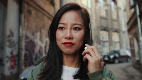 빈민가의 좁은 거리를 걷고 있는 젊고 아름다운 세련된 소녀를 가까이서 귀에 헤드폰을 끼고 즐겁게 음악을 들으며