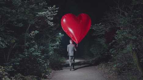 man walking in forest with a giant red heart balloon at night