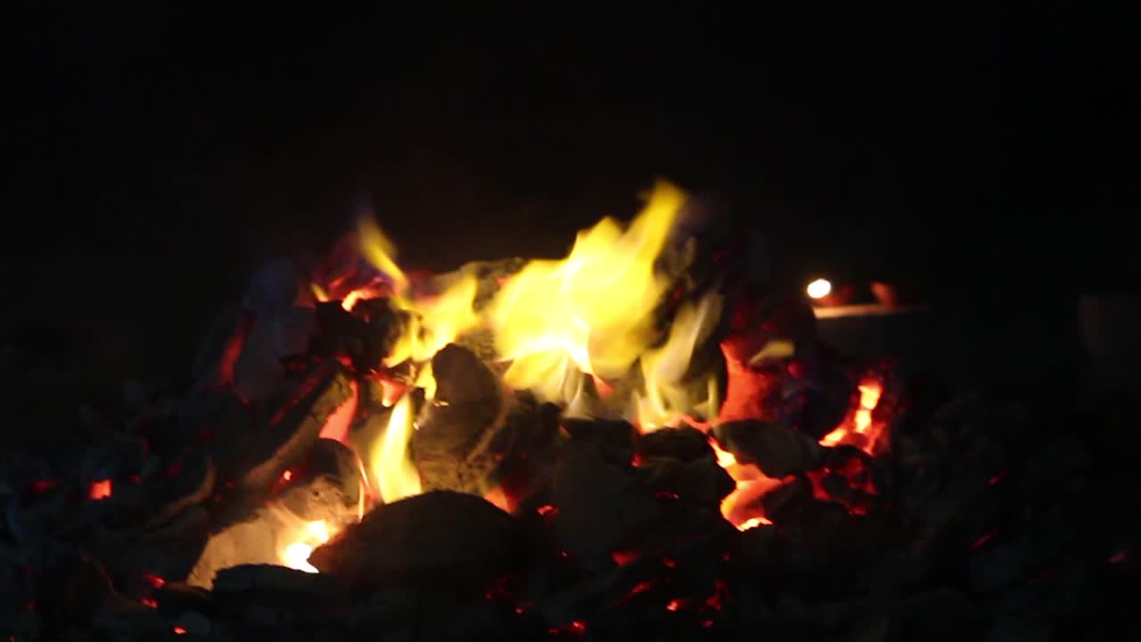 Close-up of glowing charcoal fire with yellow flames and red-hot embers. Ideal for BBQ scenes, fire texture backgrounds, grilling footage, meditation or cinematic mood visuals.