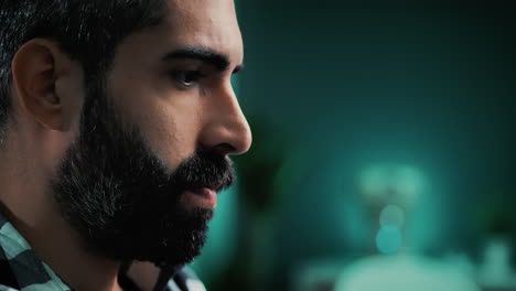 primer plano de un joven apuesto caucásico independiente con barba, trabajando con su computadora, enfocado en su proyecto e investigación mientras está sentado en la oficina de su casa