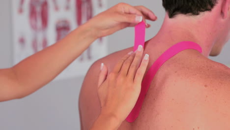 fisioterapeuta aplicando cinta kinesio rosada en la espalda de los pacientes varones