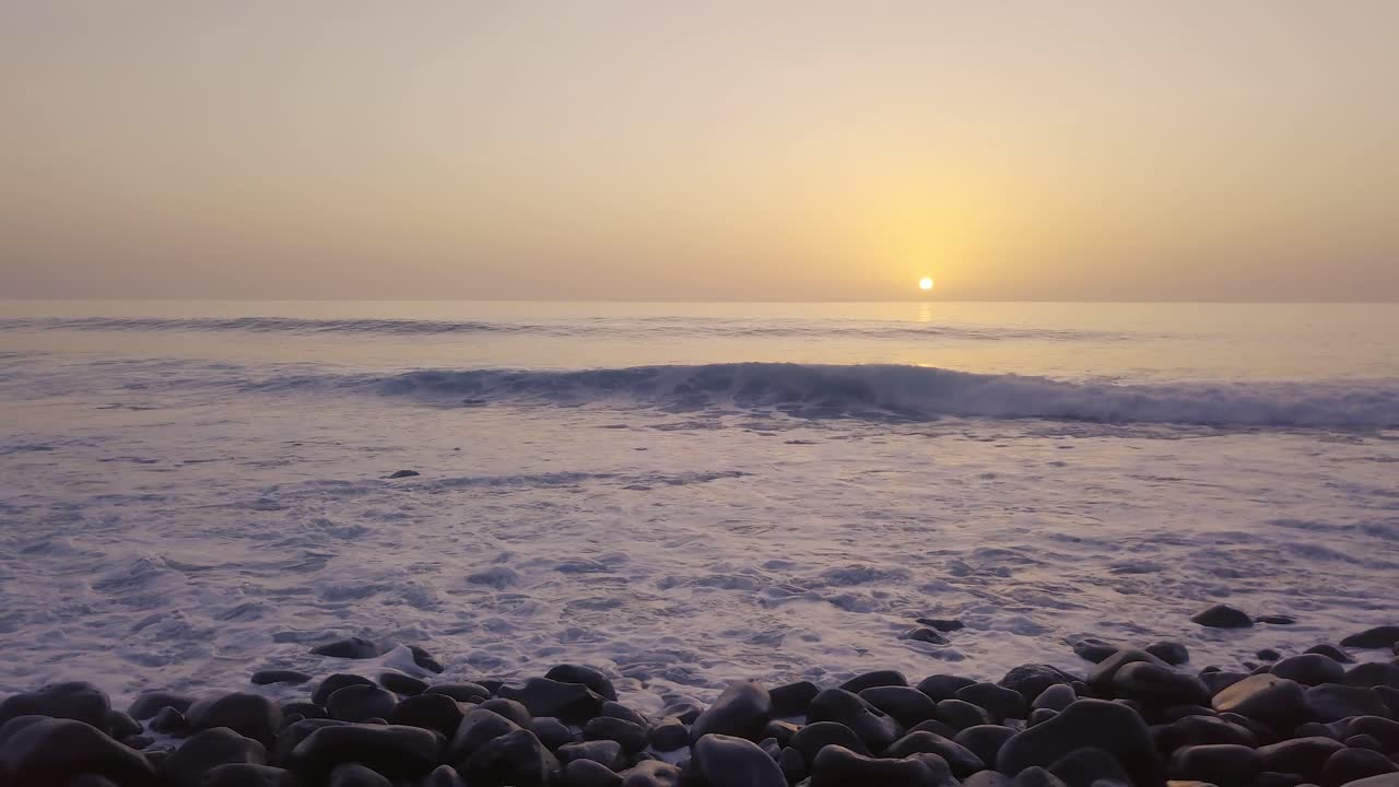 전경에 작은 파도가 있는 바위 해변 위에 놀랍도록 빛나는 오렌지색 일몰