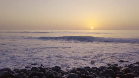 amazing glowing orange sunset over rocky beach with small waves in foreground