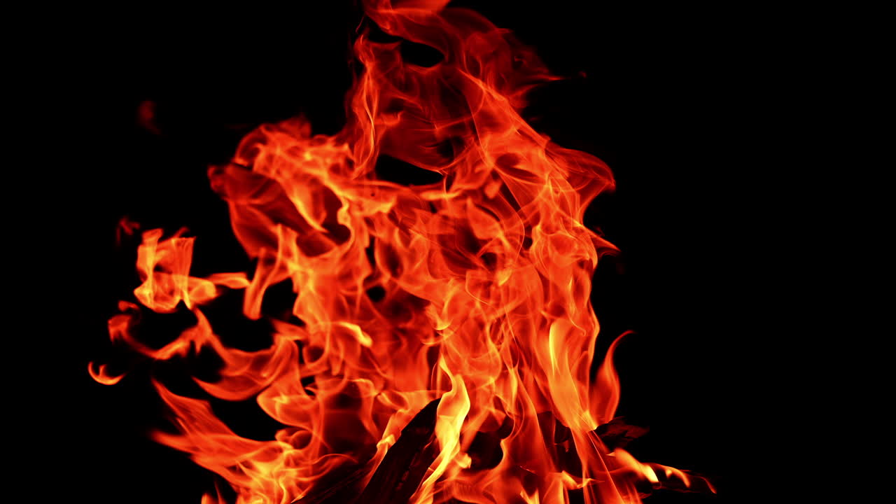 Rather large campfire burning at night. Fire flames lean to the side and tiny sparkles rise up. Isolated bonfire close up.