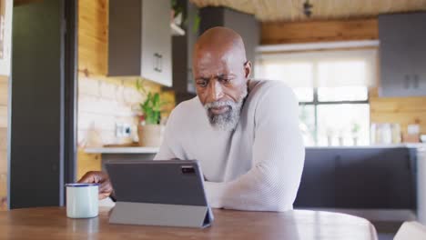 Senior-african-american-man-in-log-cabin,-using-tablet-and-drinking-coffee,-slow-motion
