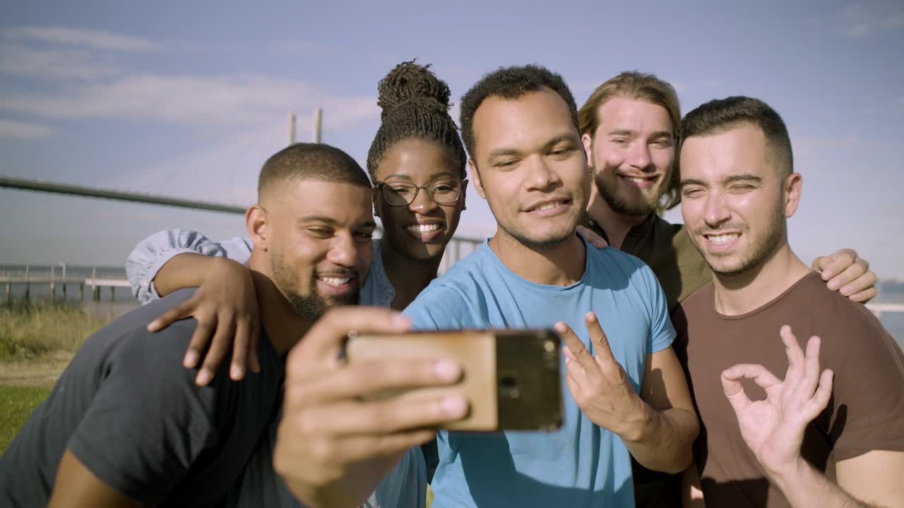 amigos sonrientes haciendo gestos mientras se toman una selfie con el teléfono inteligente