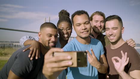 smiling friends gesturing while taking selfie with smartphone