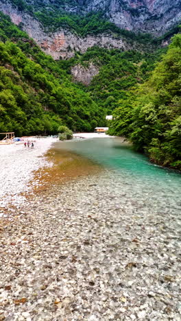 beautiful shallow river with pebble bottom. few people walk by the beach in the high mountains. vertical video.