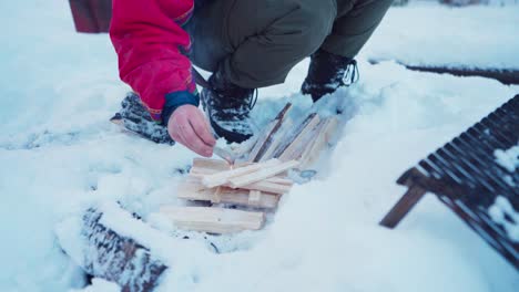 man making fire on chopped wood in the snow during winter