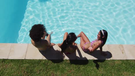 grupo diverso de amigas sentadas a la orilla de la piscina hablando