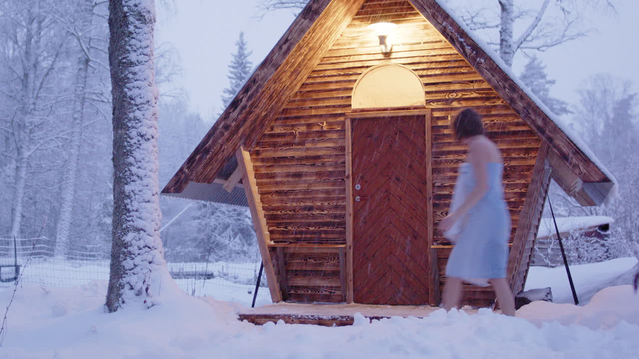 Couple on winter getaway enter wooden sauna surrounded by snow in remote woods
