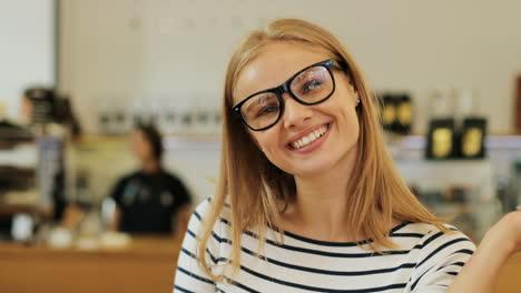 close-up view of caucasian blonde woman in glasses smiling at camera sitting at a table in a cafe