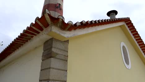 faro da barra emergiendo detrás de un techo adornado con azulejos rojos en praia da costa nova, portugal