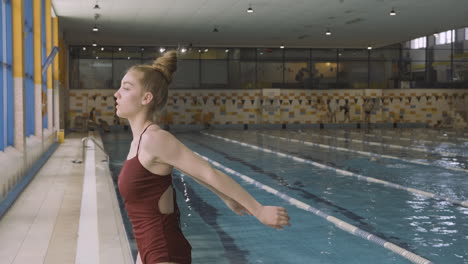 young female with her hair in a bun stretches arms and shoulders before going for a swim at the indoor pool