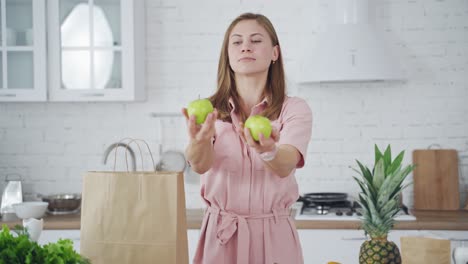 beautiful woman in light dress holding green apples. young happy female with fresh fruit looking at camera in the modern kitchen. healthy diet.