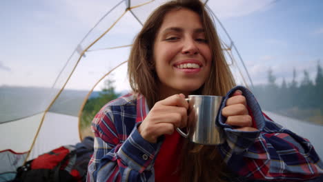 Smiling-woman-with-metal-cup-lying-down-in-tent