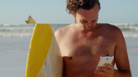 man using mobile phone while holding surfboard at beach