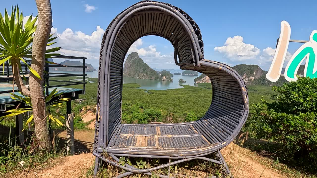 A heart-shaped structure frames a stunning view of Phuket's lush landscape and limestone formations under bright daylight