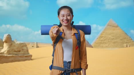 asian female hiker with mountaineering backpack smiling, touching her chest, and pointing to camera while traveling in pyramid of giza