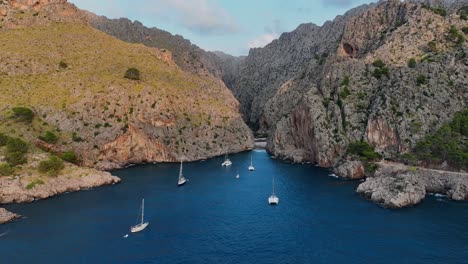 drone shot comming in towards a crack inbetween two rocks where tbvoats are anchored and there is a little beach in there. it is on mallorca.