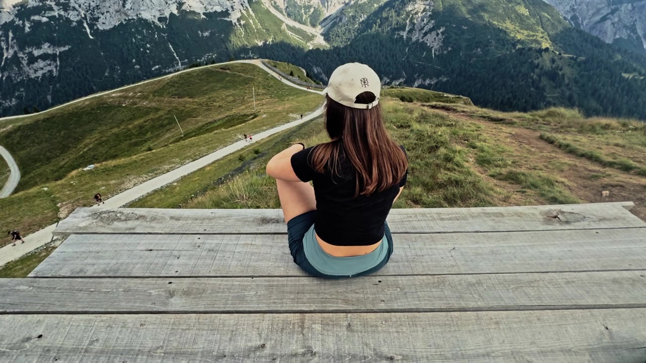 Young woman sitting on the edge of a wooden pier, contemplating the stunning alpine landscape. Scenic view of the italian dolomites from above