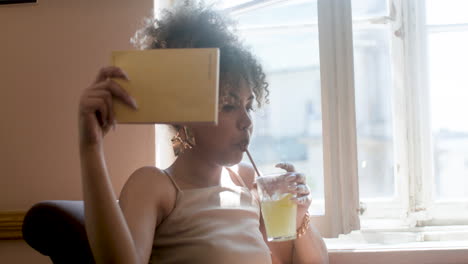 mujer africana de moda bebiendo limonada ventilándose con un libro