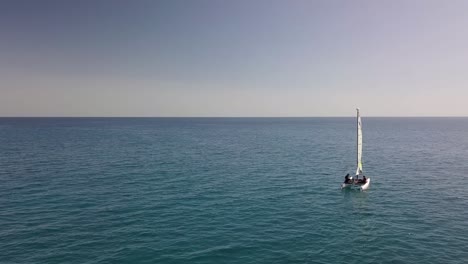 Vista-Aérea-Del-Velero-Solitario-Navegando-En-El-Agua-Del-Océano-Con-La-Cálida-Luz-Del-Atardecer