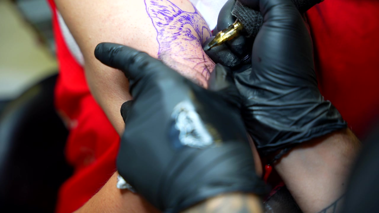 Mani di tatuatore, con guanti in nitrile neri, rimuovono l'inchiostro in eccesso dalla pelle. Primo piano