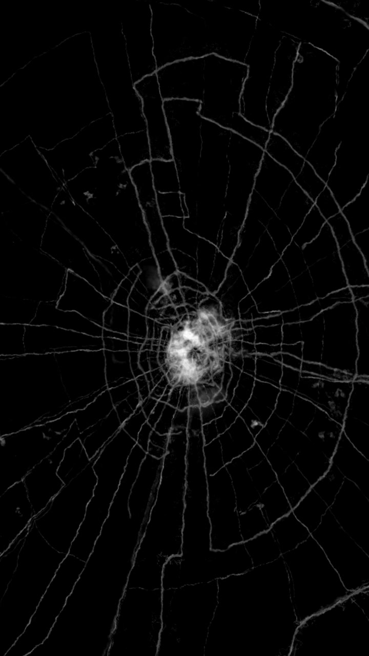 Superficie di vetro danneggiata con molteplici linee di frattura su sfondo nero, in loop continuo, formato verticale.