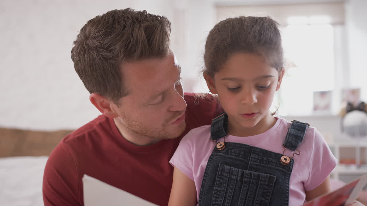 Padre e figlia in camera da letto che leggono un libro insieme