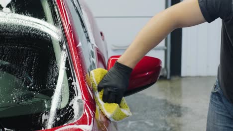 man worker washing red car on a car wash with yellow washcloth.