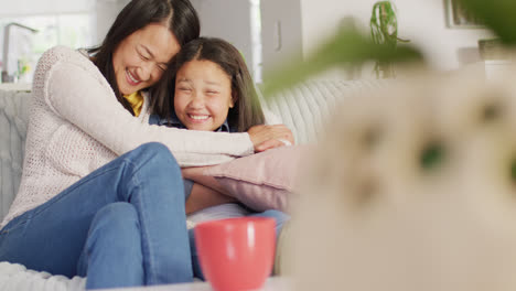 video of happy asian mother and daughter sitting on sofa and having fun