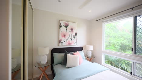 Crisp-clean-establishing-view-of-single-bed-with-ceiling-fan-and-window-overlooking-tropical-yard