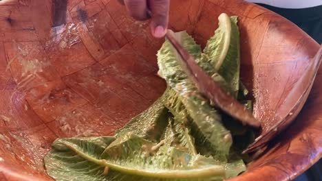 close up of lettuce leaves being mixed with a dressing to prepare caesar salad in a bowl