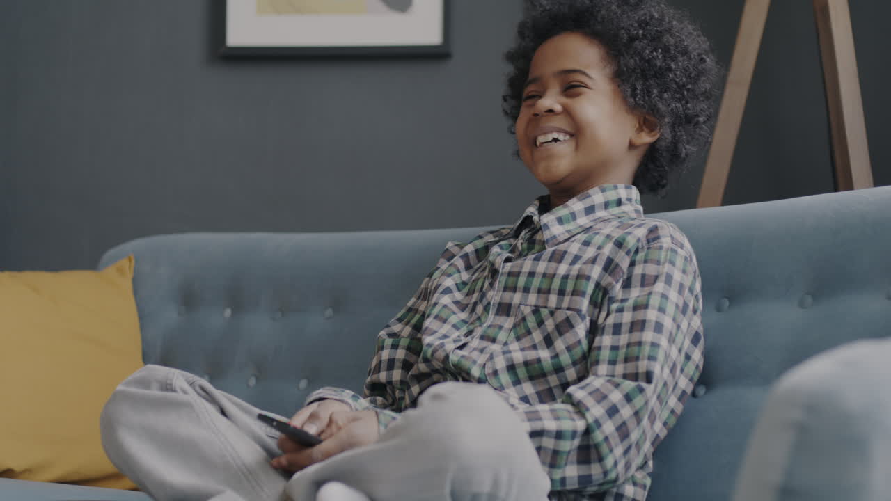 Smilende dreng ser tv på en sofa