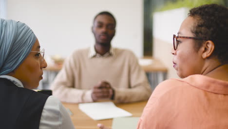 an woman and a muslim woman co workers interview a young man sitting at a table in the office 9