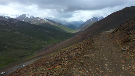 Drone-shot-rising-over-a-Tuk-Tuk-on-Babusar-pass-in-Pakistan,-with-a-few-vehicles-on-the-road-below-in-the-Kaghan-Valley,-on-a-dangerous-rocky-road