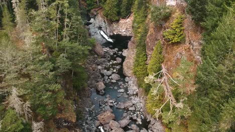 upward panning drone shot of a beautiful valley with a small river flowing through with a waterfall in the distance located in rural british colombia, canada