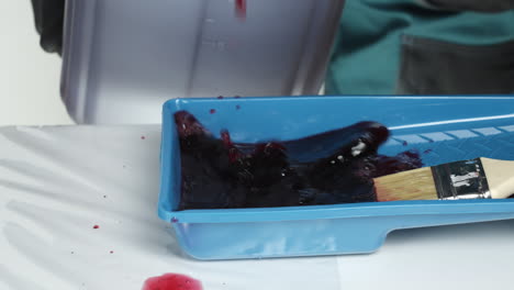 pouring red paint into a paint tray