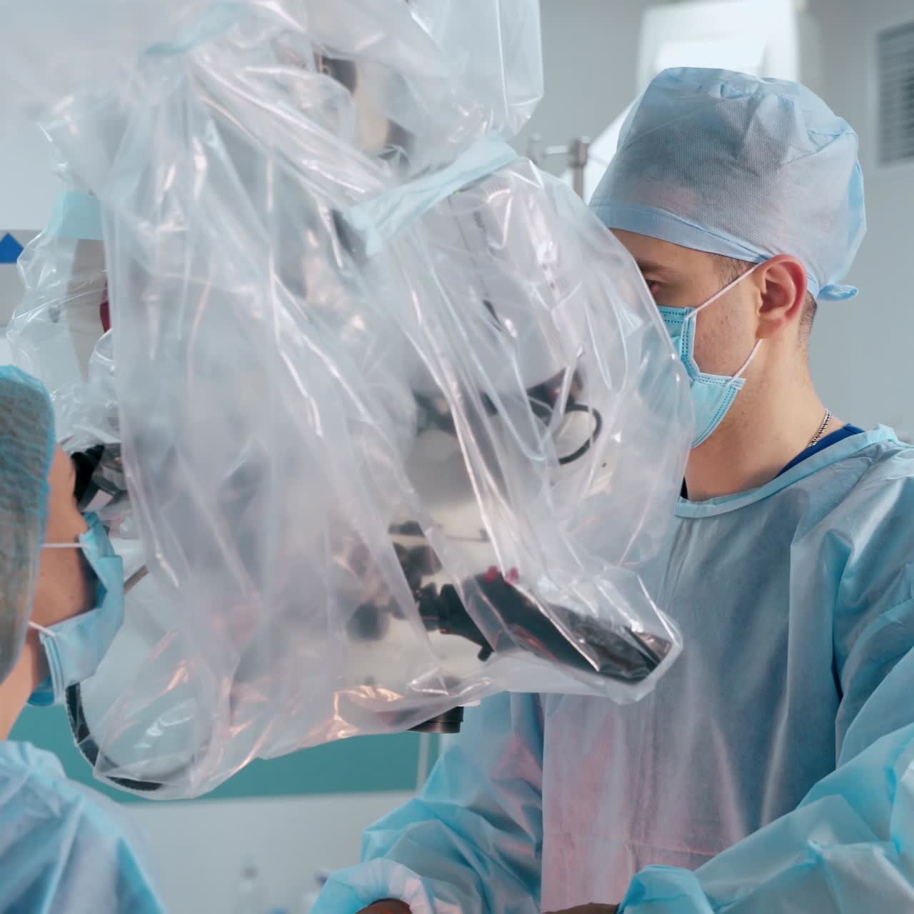 Surgeons perform a surgery through the microscope. Modern medical device in the operating room. Specialists in medical uniform during operation in hospital.