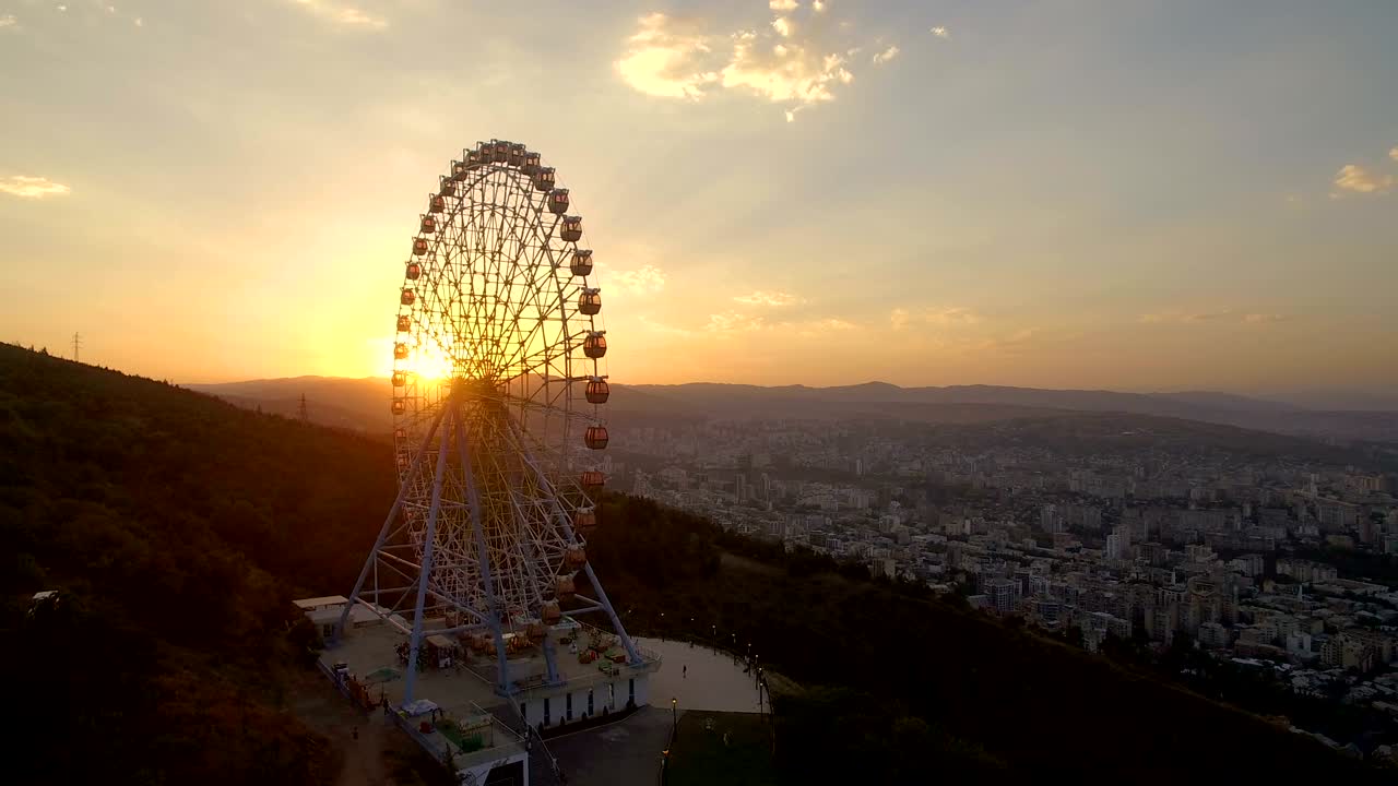 колесо обозрения и воздушный панорамный вид на город при заходе солнца