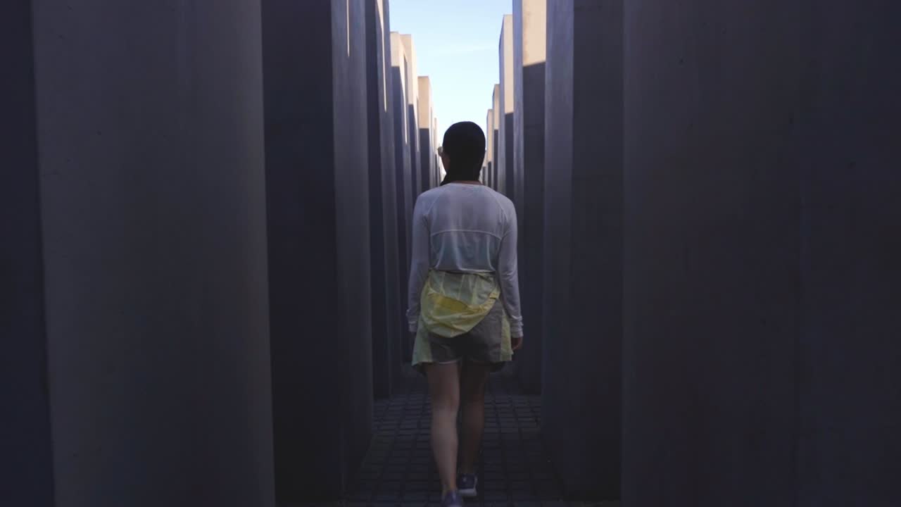 Asian woman walking through the structured labyrinth of Berlin's Holocaust Memorial, a poignant reminder of history, Berlin Germany, pullback in shadows