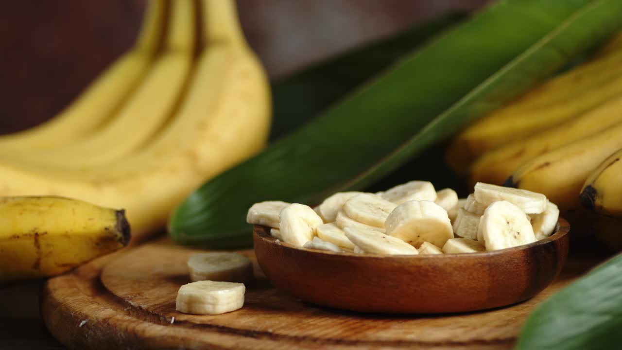 The banana slices on the plate rotate slowly with a bunch of bananas and leaves.