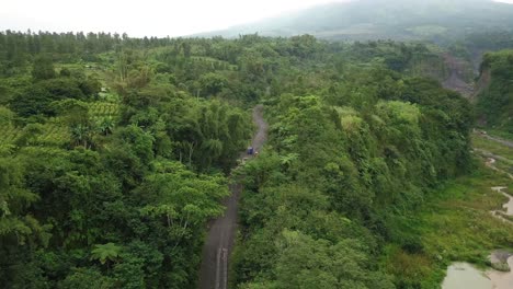 the trucks move on the road between the dense forest on the slopes of mount merapi towards the sand mines