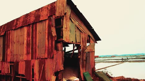 A-salt-storage-house-made-out-of-rusty-tin-with-walls-flapping-in-the-wind-in-Kampot,-Cambodia