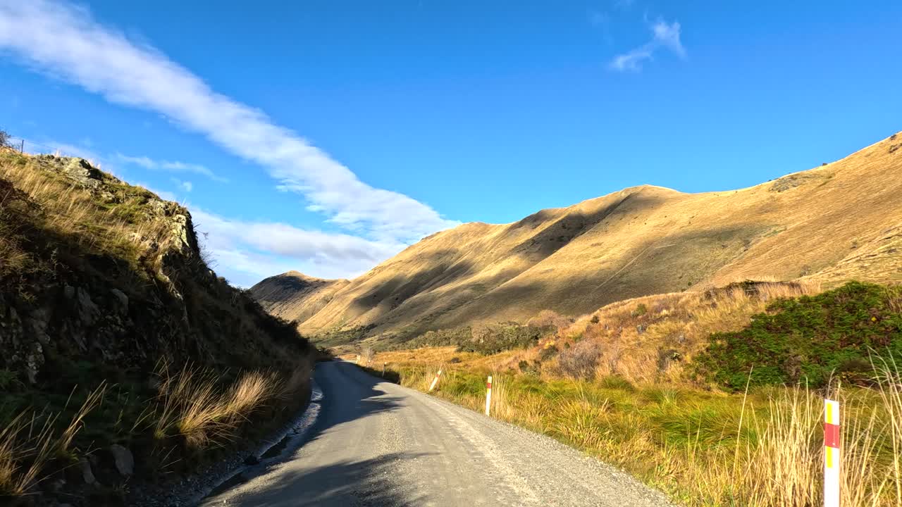 Vehicle travels scenic gravel road, sunlit hills, blue sky, wide angle, smooth forward camera movement