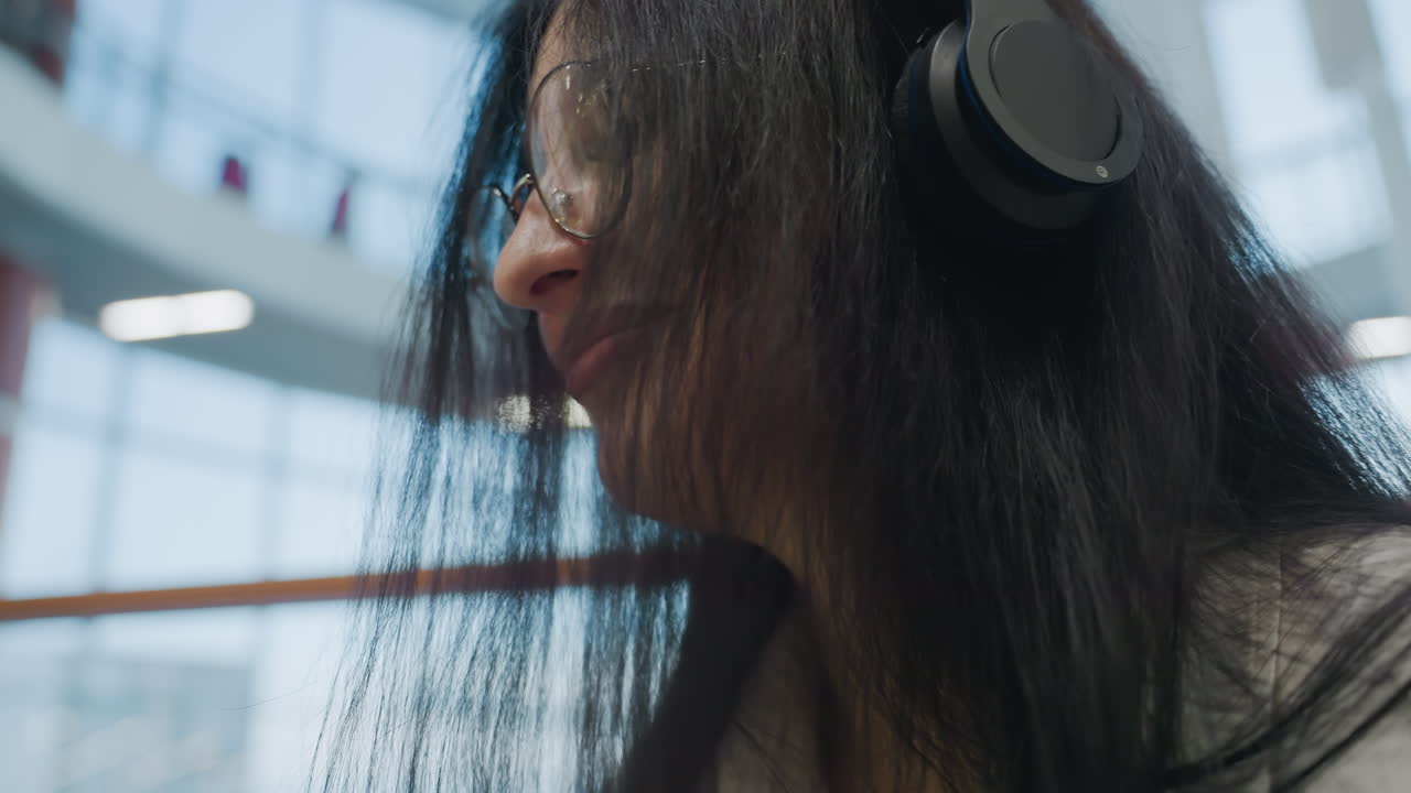 Close up of girl with long hair happily dancing to music through headset, eyes closed and smiling with joy. Bright indoor mall background