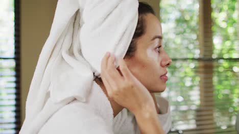 profile of happy biracial woman with vitiligo with wet hair in towel, smiling to mirror in bathroom