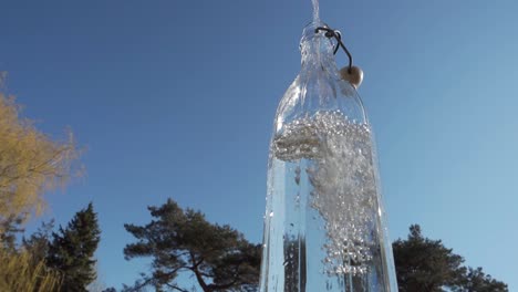 pouring water in glass bottle with blue sky and tree in background, close up, low angle