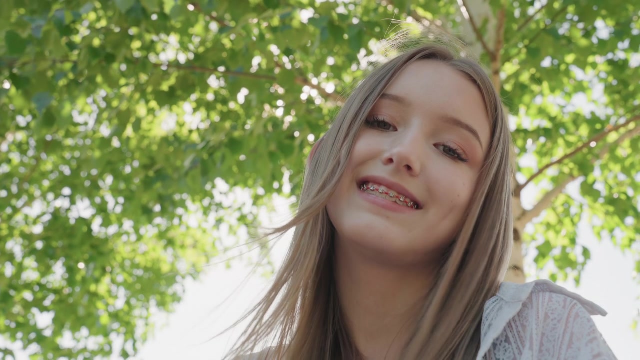 Primo piano di una giovane donna con i capelli lunghi che tiene e maneggia filati colorati in un ambiente esterno. La donna indossa abiti di pizzo di colore chiaro, concentrandosi sulle sue mani mentre lavora il materiale